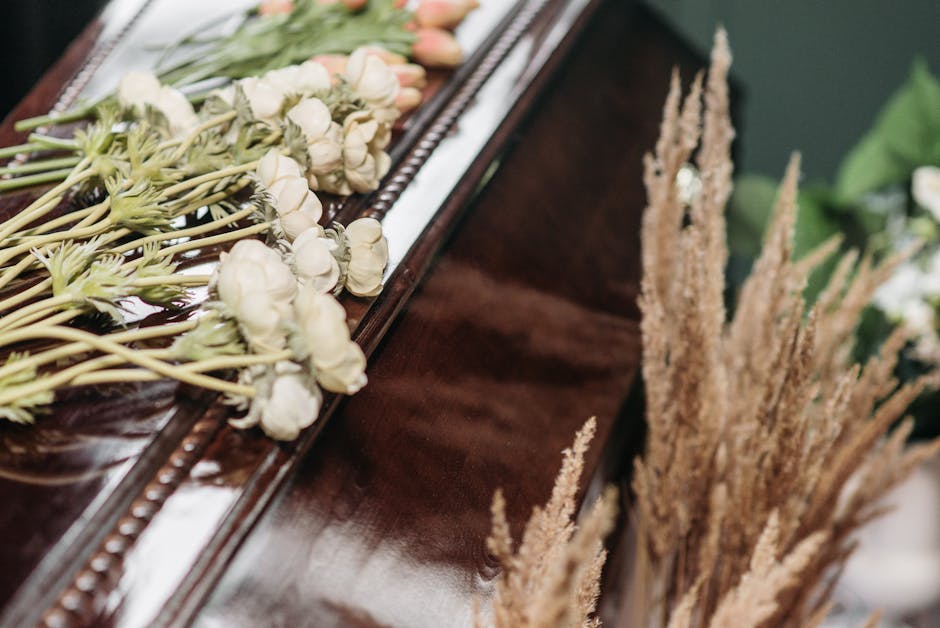 A close-up of a floral arrangement featuring white ranunculus flowers with layered petals and pale green stems, resting on a polished wooden surface. The flowers are arranged in a loose, natural style