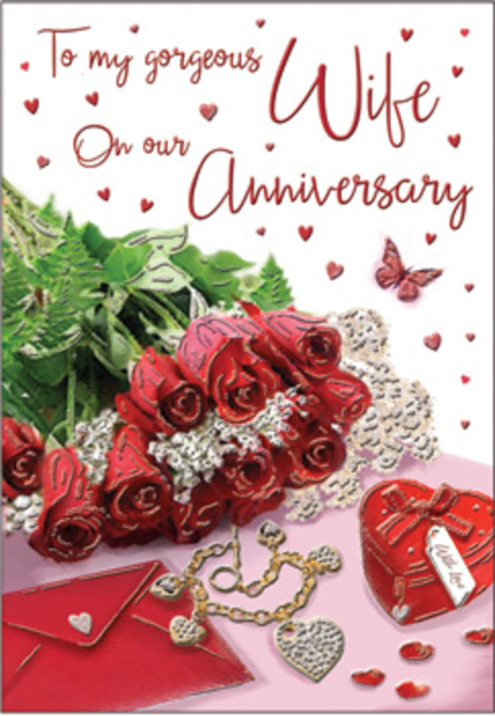 The image presents a richly detailed anniversary arrangement that feels as if it belongs on the sideboard of a Harrow home after a special evening. At the centre, a bouquet of red roses commands attention, every bloom round and generous, each petal layered like satin folds, their deep crimson colour glowing softly in the natural light. The roses are gathered with lush green foliage, the leaves creating a fresh, verdant backdrop that heightens the drama of the red, much as a Harrow florist would do when crafting a romantic bouquet for delivery around Wealdstone or near Harrow on the Hill. Surrounding this floral heart are small treasures that speak of years spent together. A vivid red box, likely a jewellery case, sits close to the flowers, its surface smooth and reflective, suggesting velvet or lacquer. Nearby, a jewellery set glints delicately, hints of gold and perhaps tiny stones catching the light in fine, precise points. Whisper-thin lace and soft heart-shaped details thread through the composition, their textures evoking fabrics worn on special occasions, or the lace trim of a cherished keepsake. The card itself is partially visible, with elegantly scripted text flowing across the surface, the curves of the letters echoing the gentle spirals of the rose petals. The background is warm and romantic, shaded in tones that complement the reds and greens without distracting from them, like the cosy interiors of neighbourhood cafés and homes across Harrow. Soft lighting, free from harsh contrasts, wraps the entire scene in a feeling of warmth and reassurance, suggesting an anniversary moment full of gratitude, shared memories, and the quiet joy of love that has grown deeper over time.